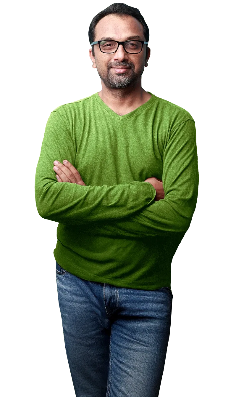 Man in a green jumper and blue jeans standing confidently, with arms crossed.