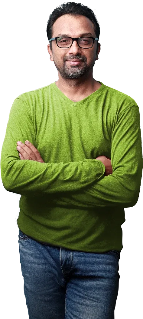 Man in a green jumper and blue jeans standing confidently, with arms crossed.